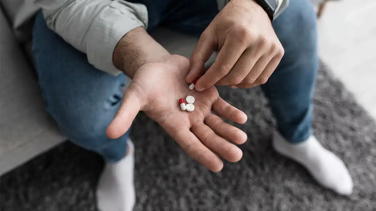 man sitting on a curb with a couple pills in his open hand