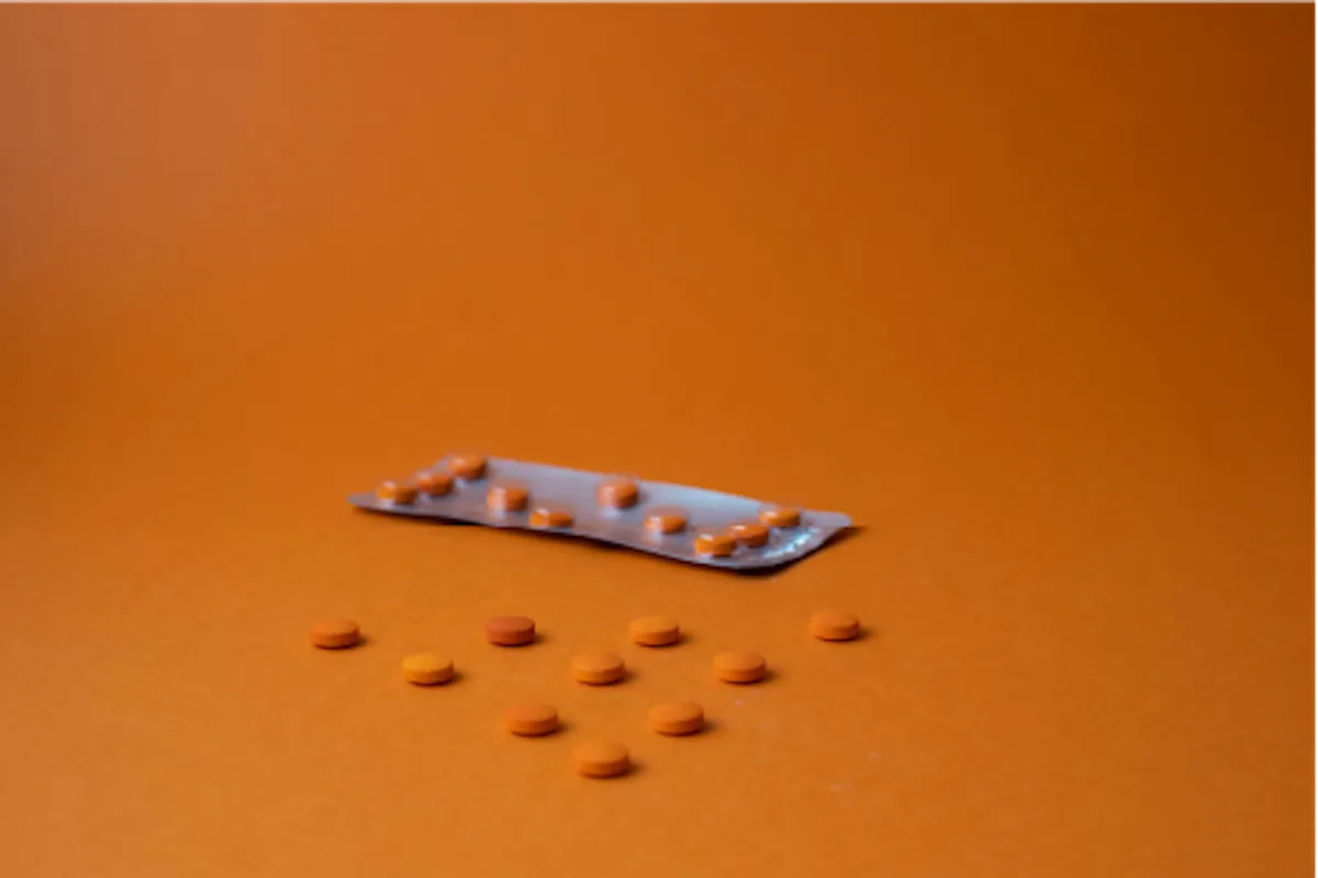 Orange pills and a blister pack on an orange background