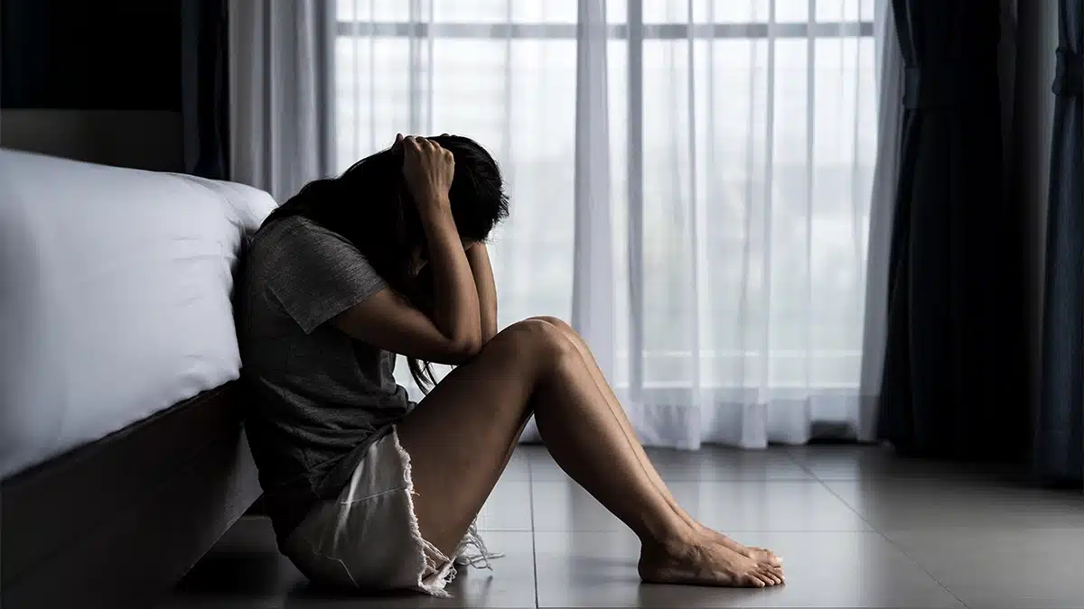 distressed woman sitting on the floor with her head down and hear hands on her head