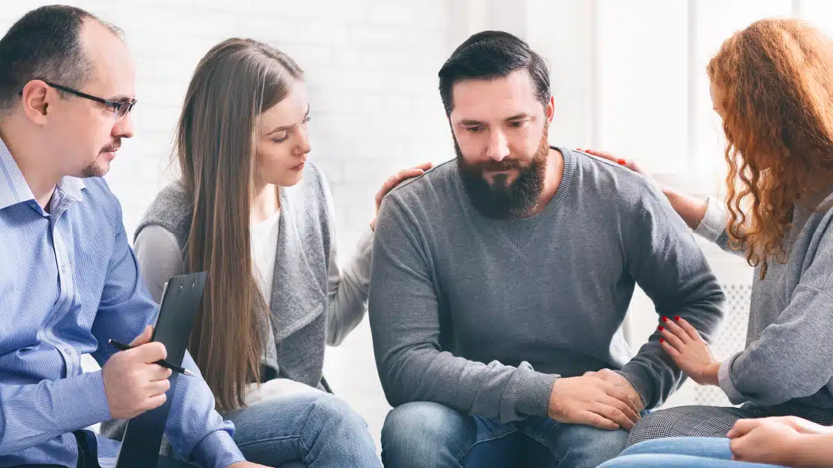 a group of people comforting a man in a therapy session