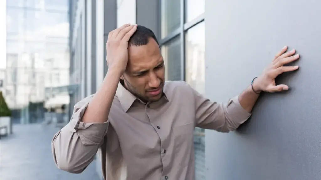 Man in distress pressing his hand on his head as he as the other hand on a wall