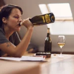 Person drinking wine straight from the bottle. Graphic lists long-term dangers of binge drinking, including heart problems and liver damage.