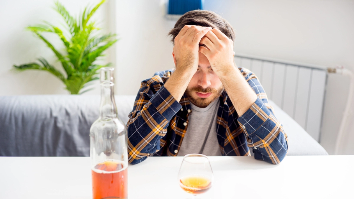 Man covering his face in front of an empty bottle of wine. Text explains an addictive personality may predispose individuals to addiction.