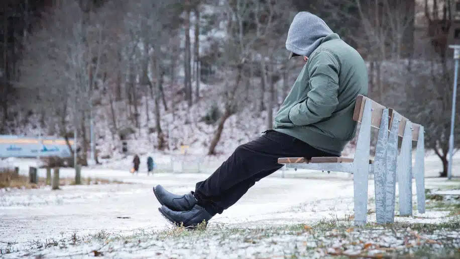 kid sitting lonely with head down on a bench in the winter snow