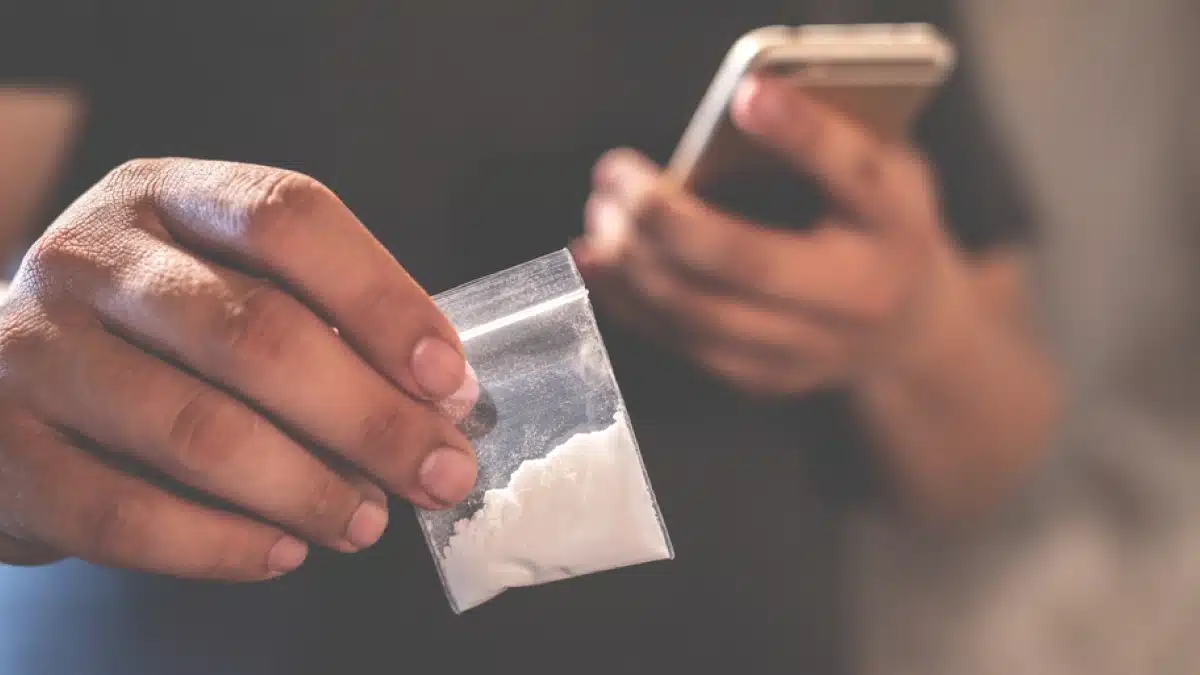 Man holding a small cocaine bag in one hand and a cell phone in the other.