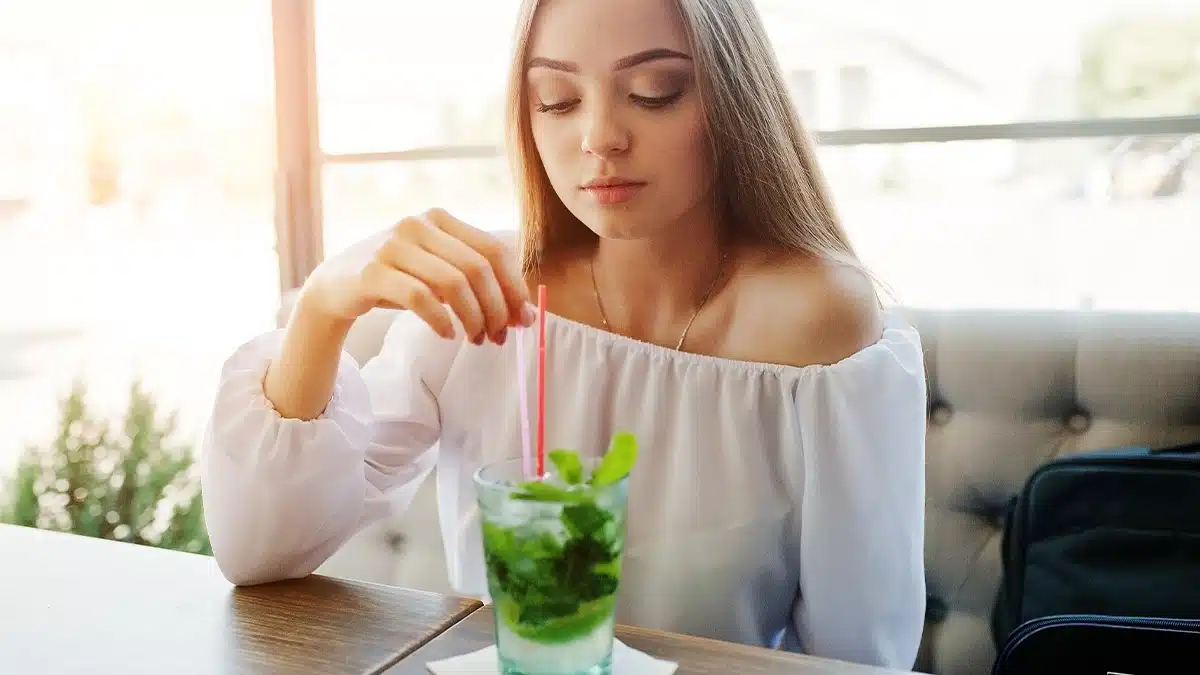 a young woman sitting at a table, gently stirring a drink with a straw.