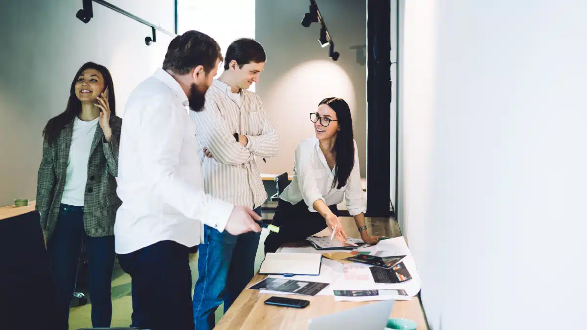 a group of four colleagues engaged in a discussion around a long table in an office setting.