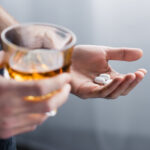 A person holding a cup of alcohol with drugs in his other hand