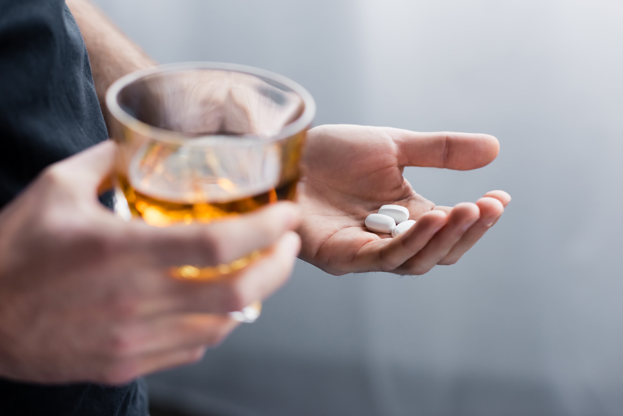 A person holding a cup of alcohol with drugs in his other hand