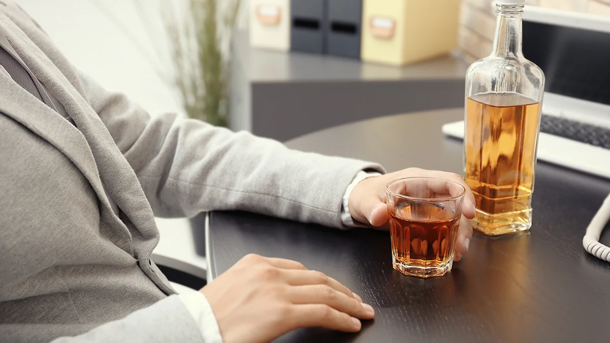 a man at a desk with a glass of alcohol