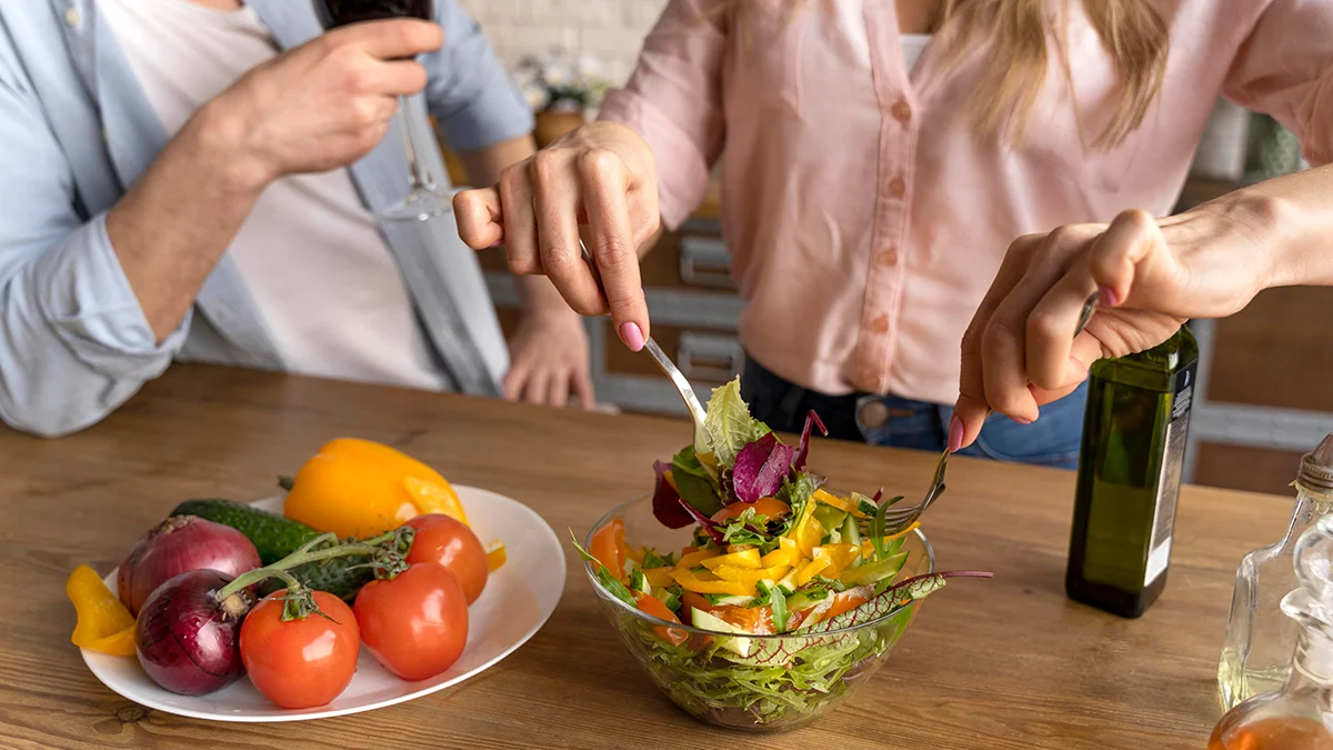 two people preparing a fresh vegetable salad in a kitchen.