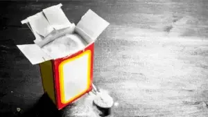 An open box sits on a dark surface, with white powder spilling out onto the table and a spoon resting nearby.