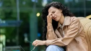 A woman with a migraine pressing her fingers on her temple.