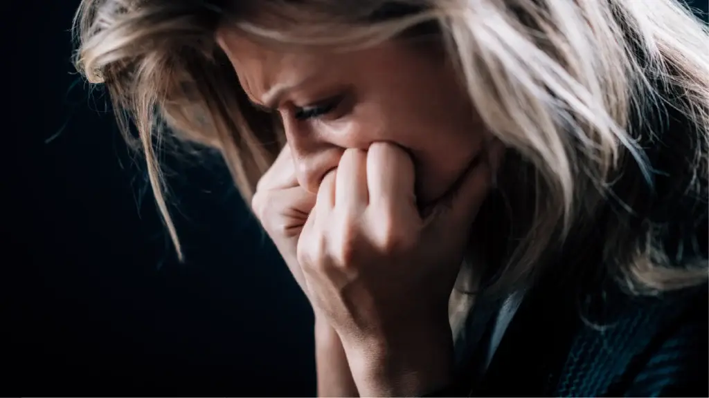 A close-up of a distressed woman with blonde hair, her face partially hidden by her hands. Her expression suggests emotional pain or anxiety