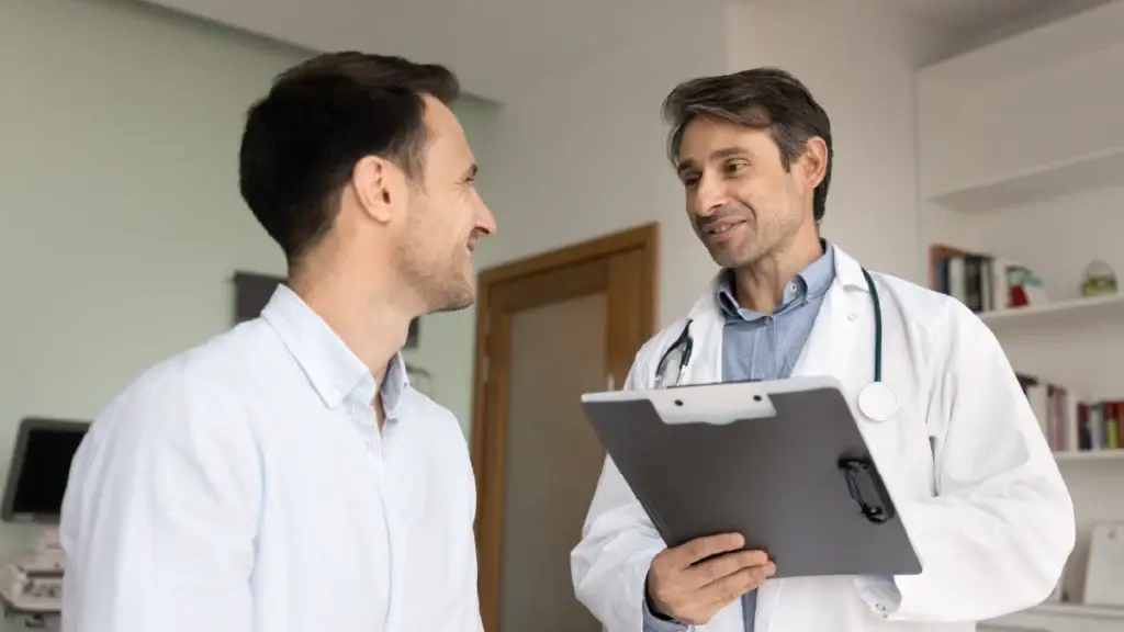 Doctor happily talking to his patient with a clipboard in his hand