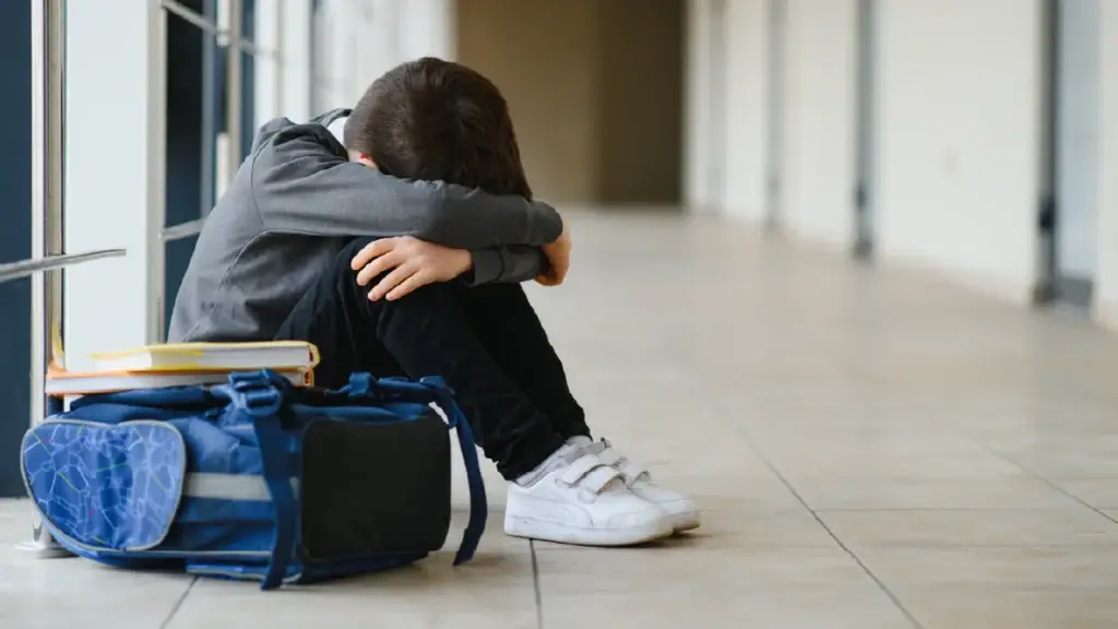 A saddened kid sitting on the floor with his head between his legs