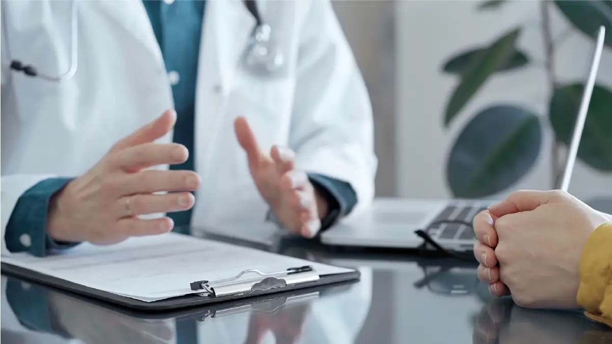 A doctor with open hands resting onclipboard, with the hands of his patient clasped together