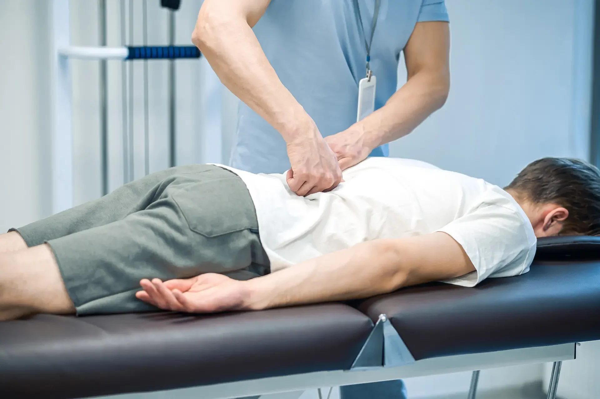 A manual therapist performs a back massage on a patient lying on a table.