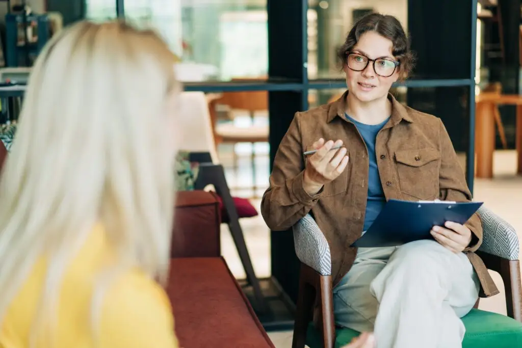 Female counselor holding a clipboard and pen, listening attentively to a client during a one-on-one session