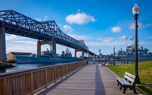 Boardwalk view in Fall River, Massachusetts with bridge and river under blue sky.