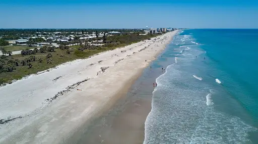 Aerial view of wide sandy beach with waves along the shoreline.