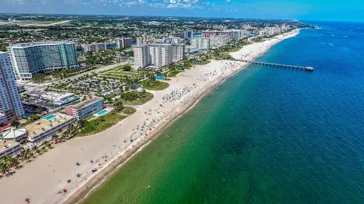 Vista aérea de una ciudad en primera línea de playa con edificios altos, playa de arena y agua turquesa.