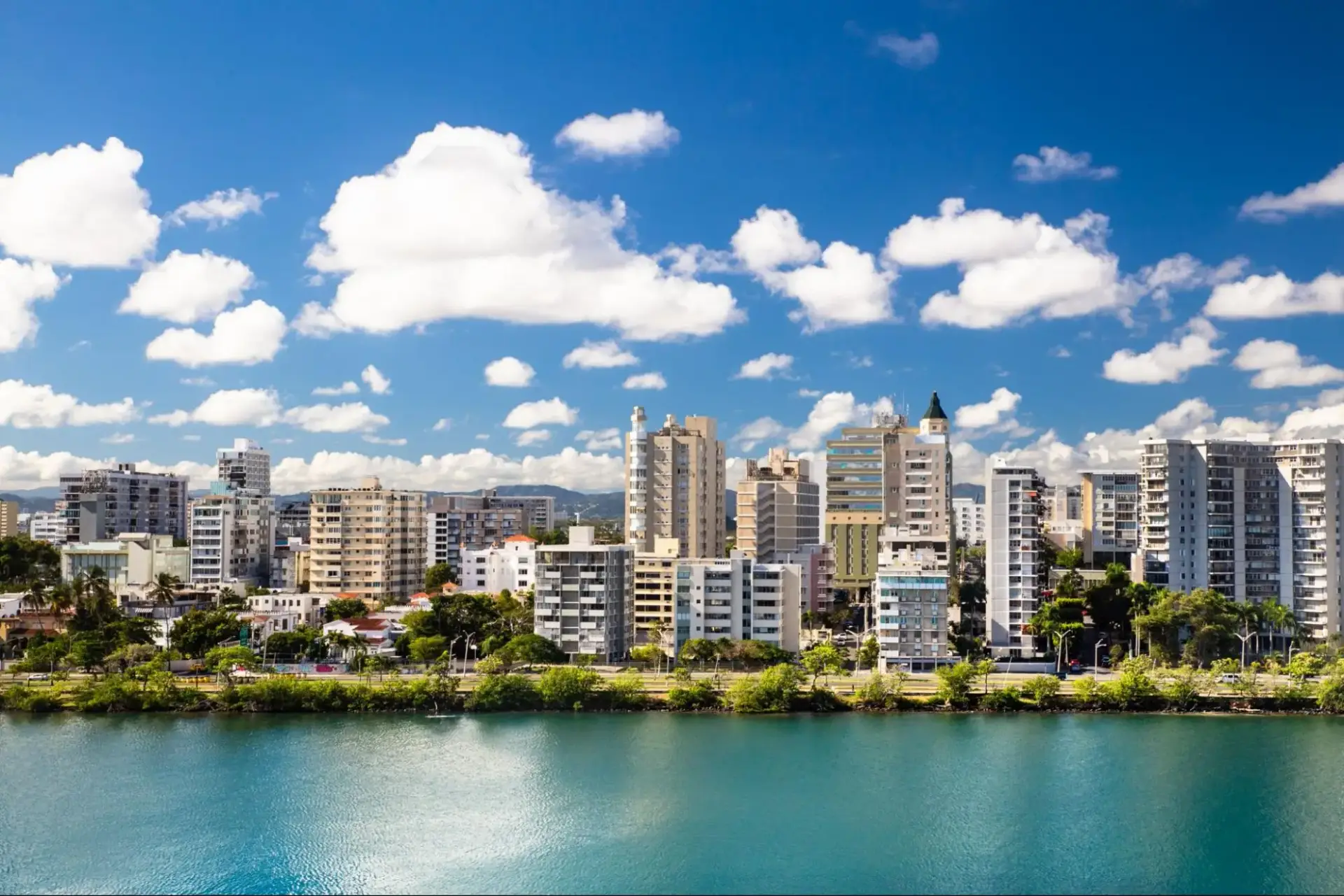 Cityscape of San Juan, Puerto Rico with modern buildings under a blue sky, viewed across the water.
