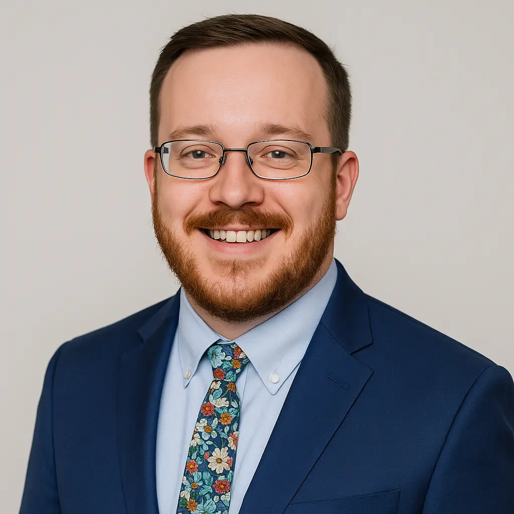 Fotografía de Zachary Gaboriault con gafas y traje azul con corbata estampada, sonriendo.
