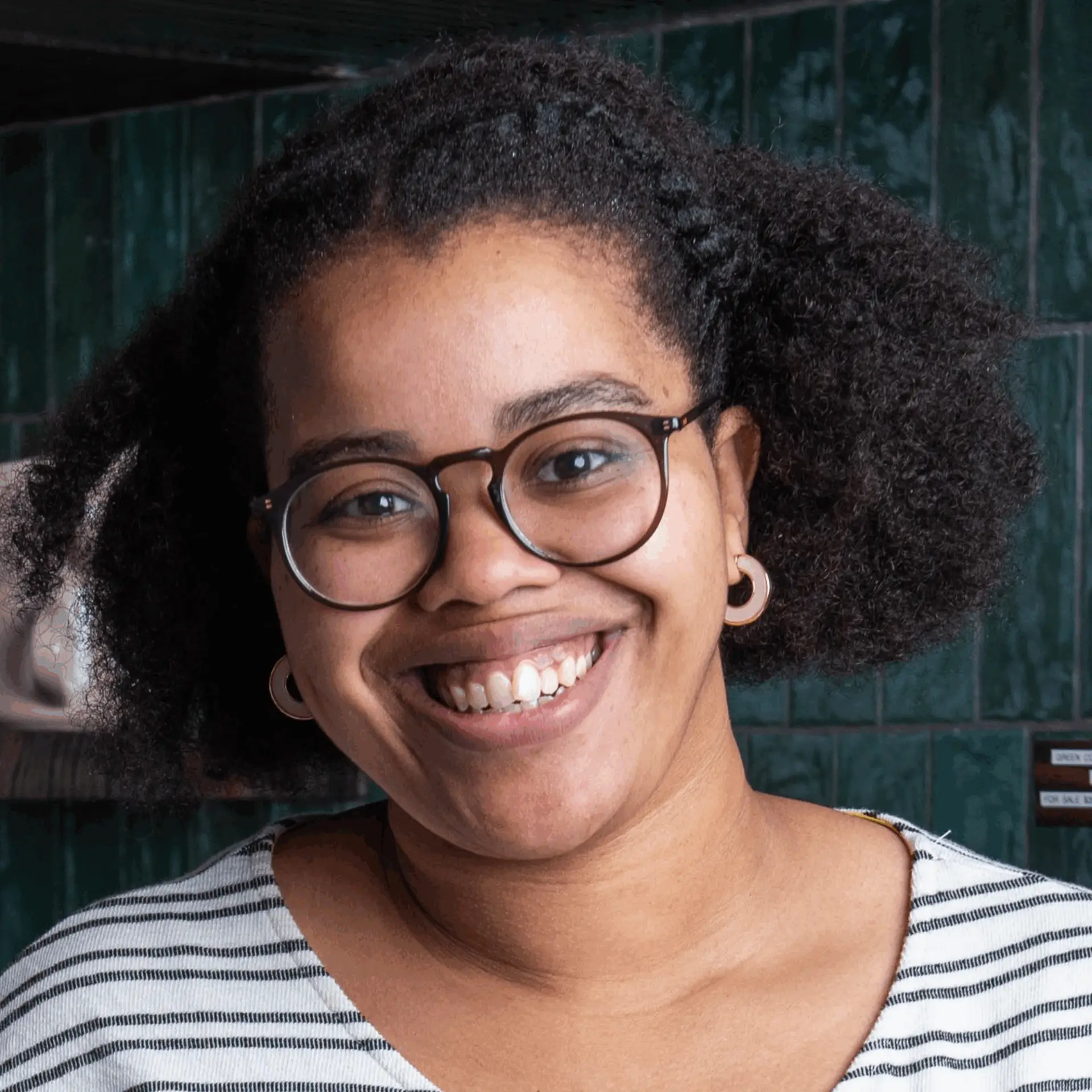 A smiling woman with curly hair and glasses poses for a portrait.