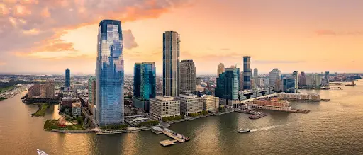 City skyline with skyscrapers reflecting on water at sunset.