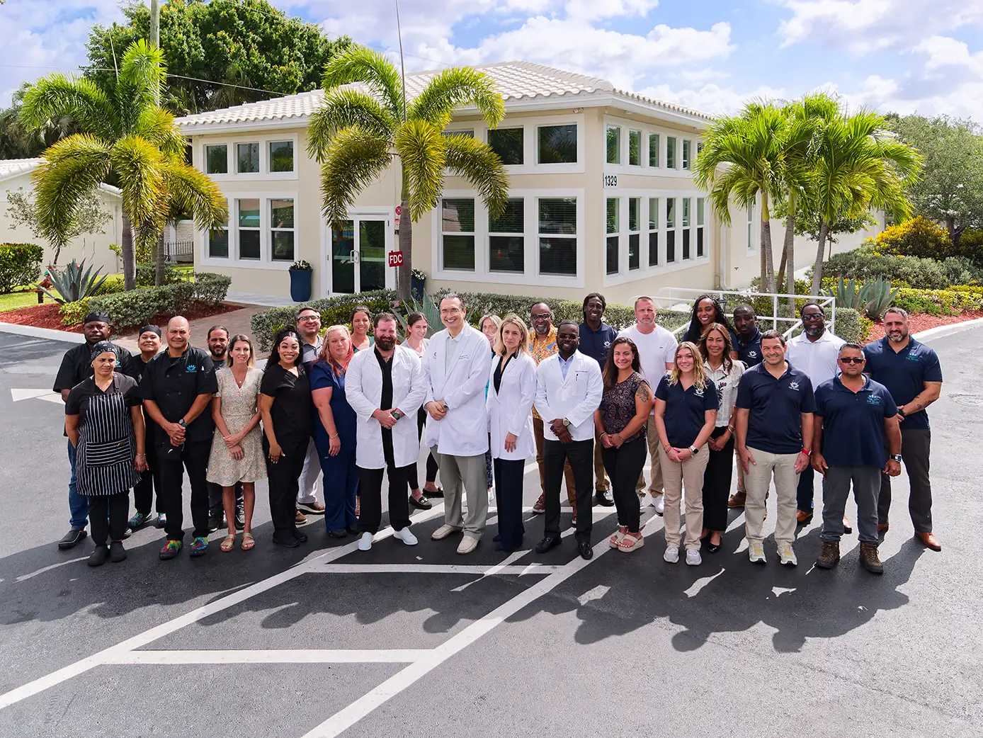 Group photo of The Haven Detox Florida team standing together outside the treatment center building on a sunny day, with palm trees and the facility’s white exterior in the background.