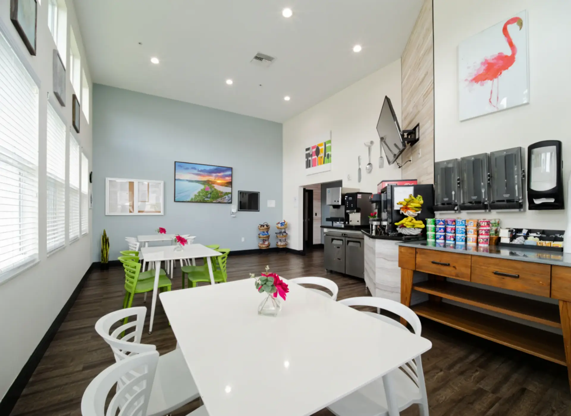 Bright patient café with white tables and green chairs, featuring a snack and beverage station in a modern treatment facility.